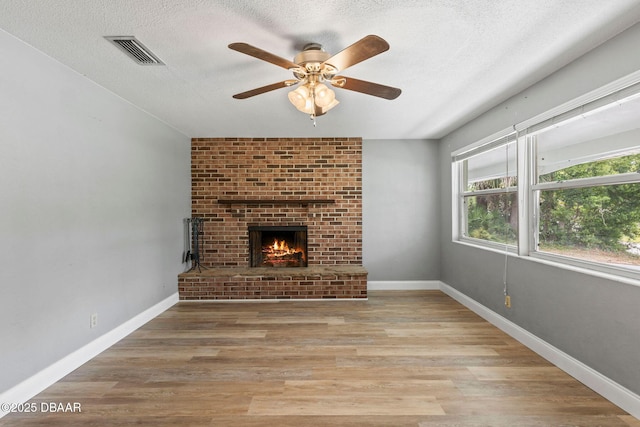 unfurnished living room with a fireplace, a ceiling fan, light wood-style floors, a textured ceiling, and baseboards