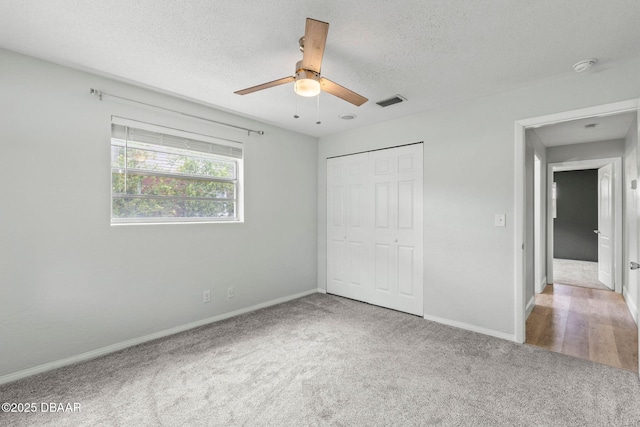 unfurnished bedroom with carpet, baseboards, a closet, ceiling fan, and a textured ceiling