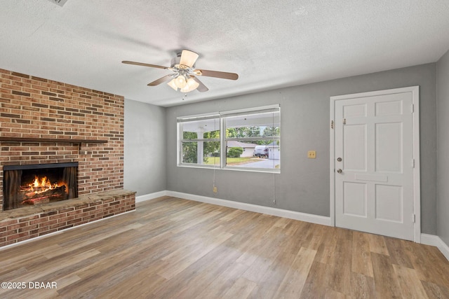 unfurnished living room featuring wood finished floors, a textured ceiling, a ceiling fan, a fireplace, and baseboards