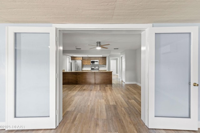 kitchen featuring stainless steel appliances, wood finished floors, a ceiling fan, a peninsula, and baseboards