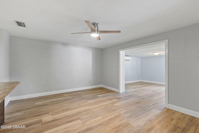 unfurnished room with a ceiling fan, light wood-type flooring, baseboards, and a wall unit AC
