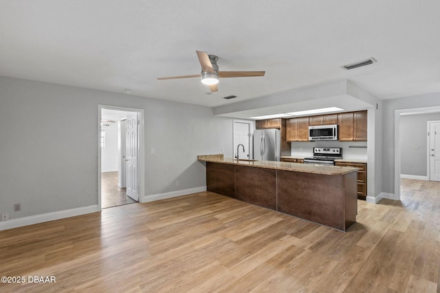 kitchen with appliances with stainless steel finishes, a peninsula, a ceiling fan, and baseboards