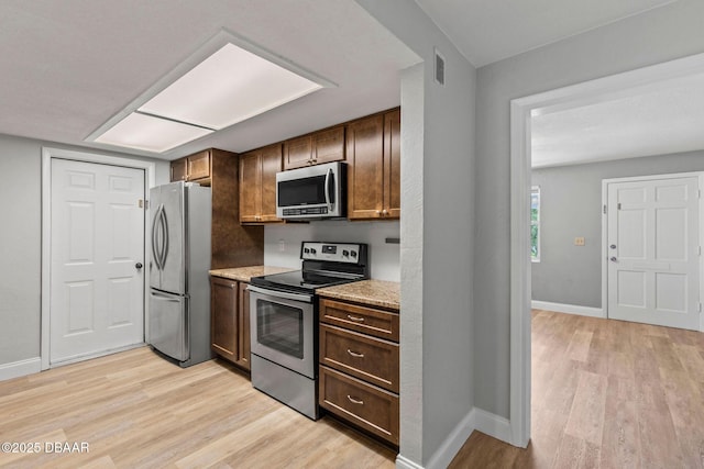 kitchen with stainless steel appliances, light wood-style flooring, baseboards, and light stone countertops