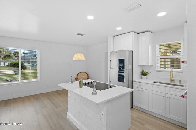 kitchen with black electric cooktop, a kitchen island, sink, white cabinets, and stainless steel refrigerator