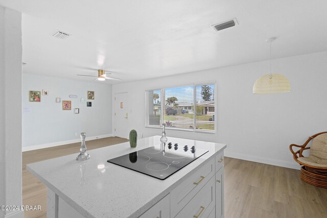 kitchen featuring pendant lighting, black electric stovetop, light wood-type flooring, light stone counters, and white cabinetry