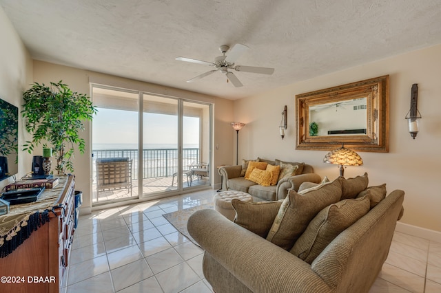 living room featuring ceiling fan, a textured ceiling, light tile patterned floors, and a water view