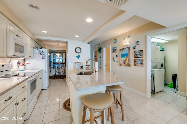 kitchen featuring sink, a breakfast bar area, stacked washer / dryer, a kitchen island with sink, and white appliances