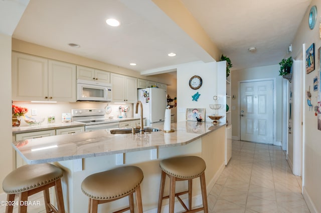 kitchen with kitchen peninsula, a breakfast bar area, sink, light stone countertops, and white appliances