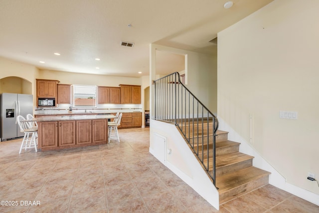 4690 S Atlantic Ave, Ponce Inlet, FL 32127 - kitchen with stainless steel fridge with ice dispenser, black microwave, a breakfast bar, a center island, and brown cabinetry