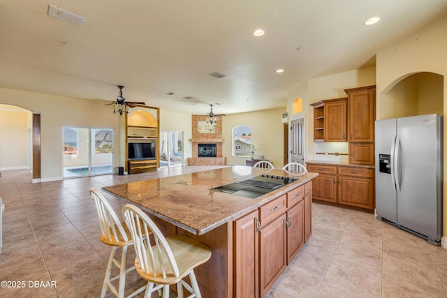 4690 S Atlantic Ave, Ponce Inlet, FL 32127 - kitchen featuring stainless steel fridge, black electric cooktop, brown cabinetry, open floor plan, and a fireplace