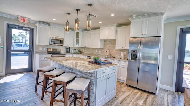 kitchen featuring white cabinetry, crown molding, hanging light fixtures, appliances with stainless steel finishes, and a kitchen island