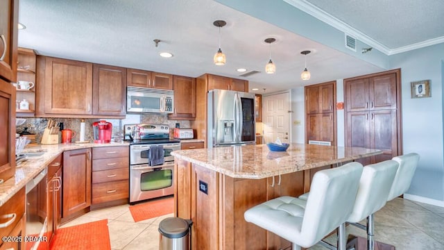 kitchen featuring a breakfast bar area, crown molding, appliances with stainless steel finishes, a kitchen island, and pendant lighting