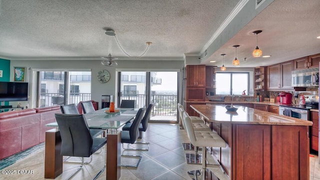 kitchen with light stone counters, light tile patterned floors, ornamental molding, appliances with stainless steel finishes, and pendant lighting