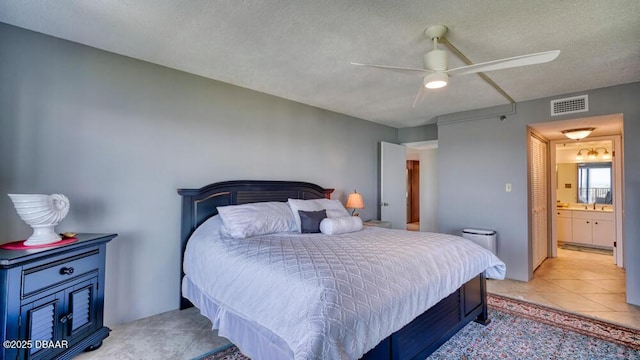 bedroom with connected bathroom, light tile patterned floors, a textured ceiling, and ceiling fan