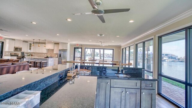 kitchen featuring appliances with stainless steel finishes, dark stone countertops, hanging light fixtures, a water view, and white cabinets