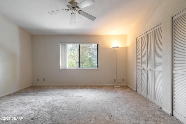 unfurnished bedroom featuring two closets, light colored carpet, and ceiling fan