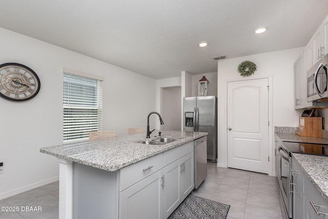 kitchen with light tile patterned flooring, sink, light stone counters, a center island with sink, and stainless steel appliances