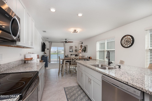 kitchen with sink, white cabinets, light tile patterned floors, light stone counters, and stainless steel appliances