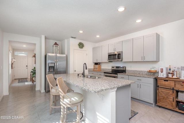 kitchen featuring sink, light stone counters, a kitchen breakfast bar, an island with sink, and stainless steel appliances