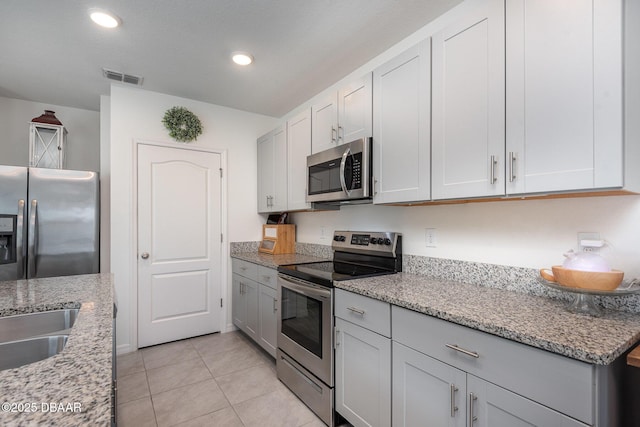 kitchen with stainless steel appliances, light stone countertops, and light tile patterned floors