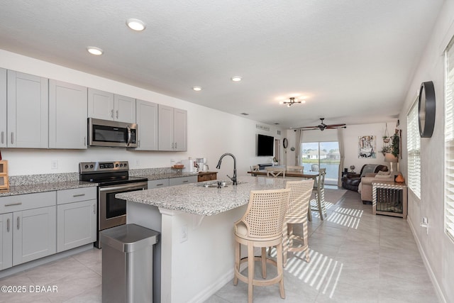 kitchen with stainless steel appliances, sink, a center island with sink, and gray cabinetry