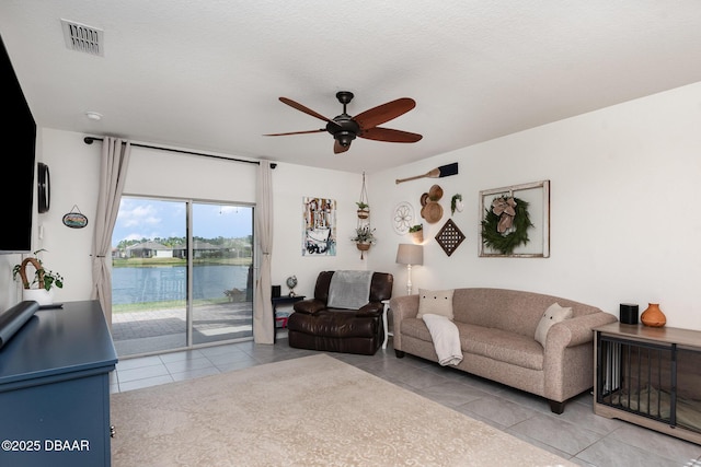 living room featuring light tile patterned floors, a textured ceiling, ceiling fan, and a water view