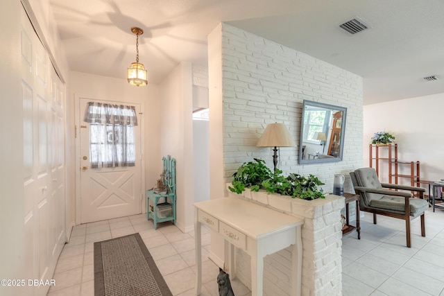 entryway with brick wall, plenty of natural light, visible vents, and light tile patterned floors