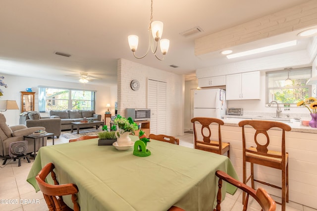 dining room with a toaster, light tile patterned floors, ceiling fan with notable chandelier, and visible vents