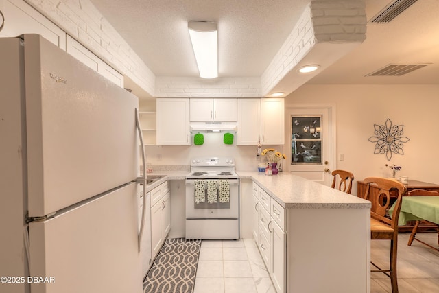 kitchen featuring visible vents, under cabinet range hood, a kitchen breakfast bar, white appliances, and a peninsula