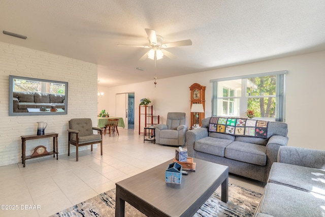 living area with light tile patterned floors, a ceiling fan, visible vents, and a textured ceiling