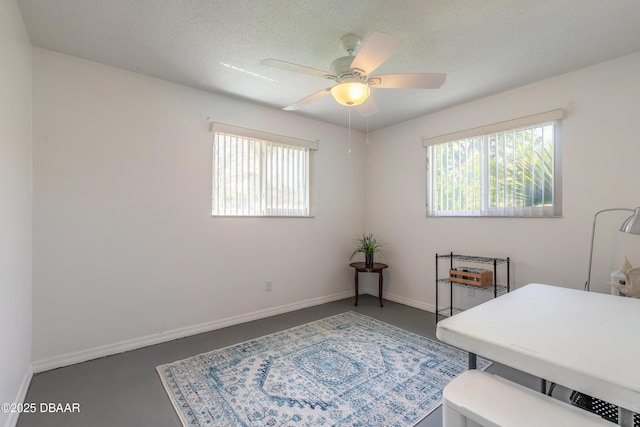 office area with a textured ceiling, baseboards, a ceiling fan, and finished concrete flooring