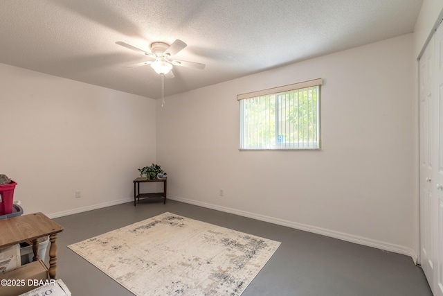 interior space featuring baseboards, a textured ceiling, concrete floors, and ceiling fan