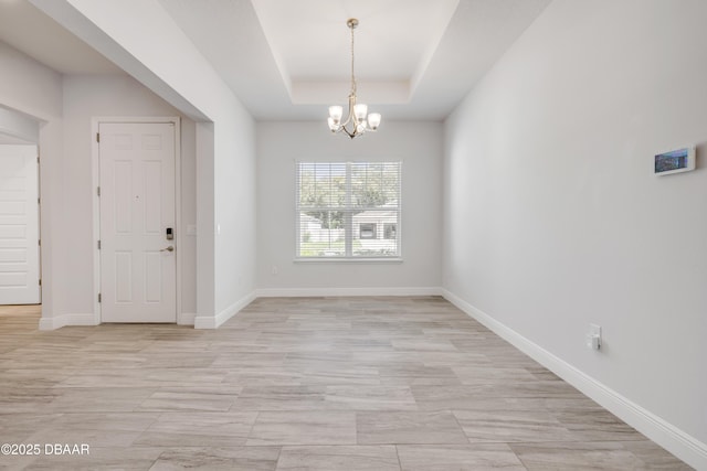 unfurnished dining area with a chandelier, a raised ceiling, and baseboards