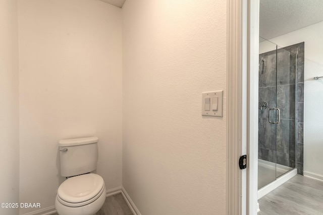 full bath featuring baseboards, a stall shower, toilet, and wood finished floors