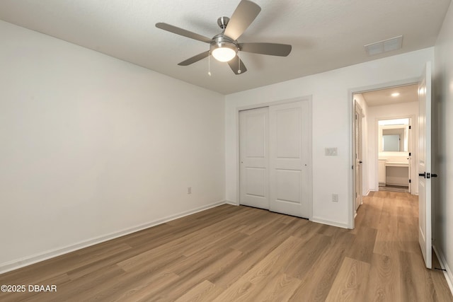 unfurnished bedroom with visible vents, light wood-style flooring, baseboards, and a closet