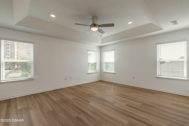empty room featuring a raised ceiling, ceiling fan, baseboards, and wood finished floors