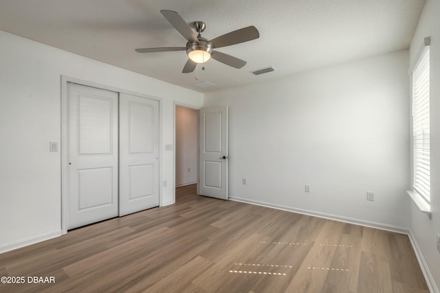 unfurnished bedroom with a ceiling fan, visible vents, wood finished floors, baseboards, and a closet