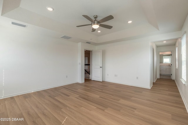unfurnished bedroom with baseboards, a tray ceiling, light wood-type flooring, and visible vents