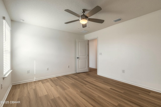 unfurnished room featuring a textured ceiling, a ceiling fan, baseboards, wood finished floors, and visible vents