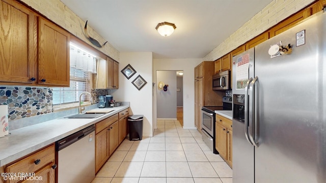 kitchen with sink, brick wall, backsplash, light tile patterned flooring, and appliances with stainless steel finishes