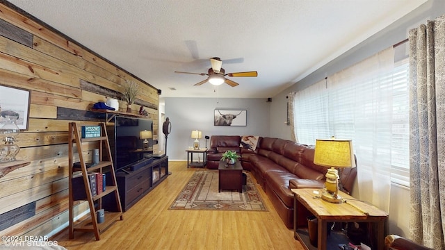 living room featuring a textured ceiling, light hardwood / wood-style flooring, ceiling fan, and wood walls