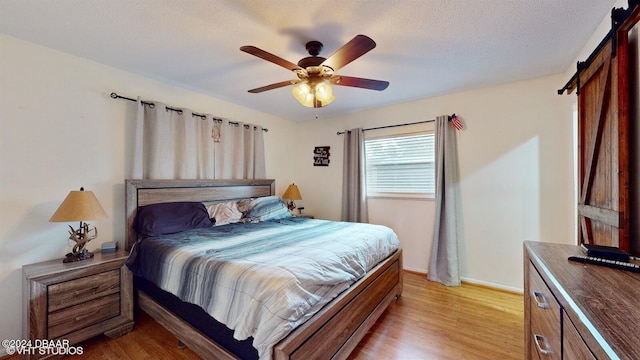 bedroom with ceiling fan, a barn door, a textured ceiling, and light hardwood / wood-style flooring