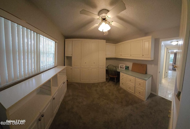 kitchen with dark colored carpet, built in desk, white cabinets, and a textured ceiling