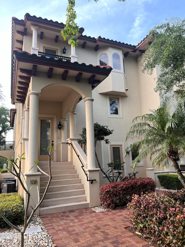 entrance to property with a tile roof, a balcony, and stucco siding