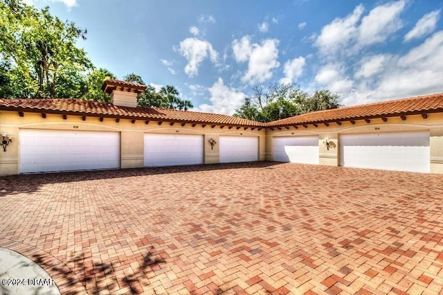 exterior space featuring a chimney, a tile roof, community garages, and stucco siding