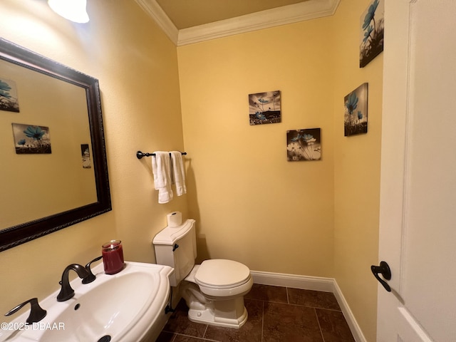 half bathroom with baseboards, toilet, tile patterned flooring, crown molding, and a sink