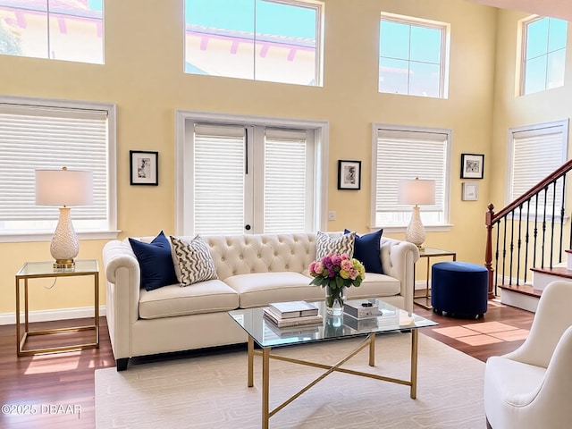 living room featuring light wood-style floors, baseboards, stairway, and a high ceiling