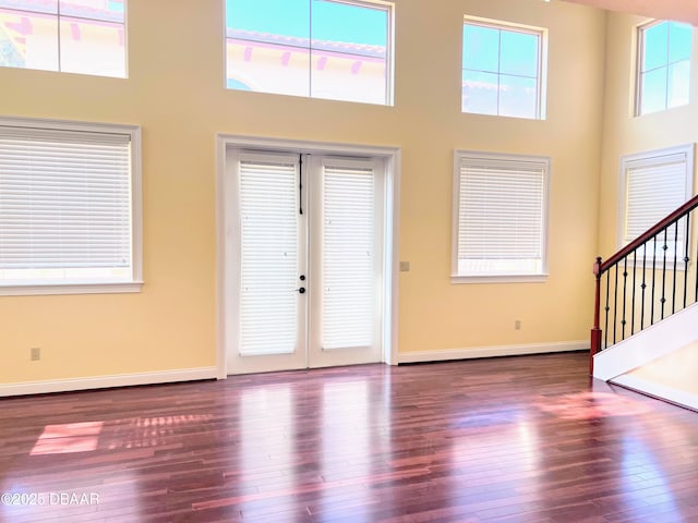 foyer entrance with baseboards, a towering ceiling, stairway, hardwood / wood-style floors, and french doors