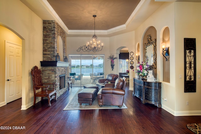 living room featuring ornamental molding, dark hardwood / wood-style floors, an inviting chandelier, a tray ceiling, and a brick fireplace