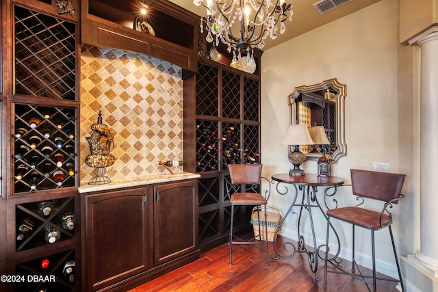 wine cellar with ornate columns, dark wood-type flooring, bar area, and a notable chandelier